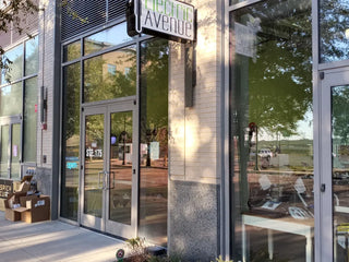 Front exterior of a retail storefront with large glass windows and double glass doors. A hanging sign reads 'Electric Avenue,' and a brick-and-glass facade is visible.